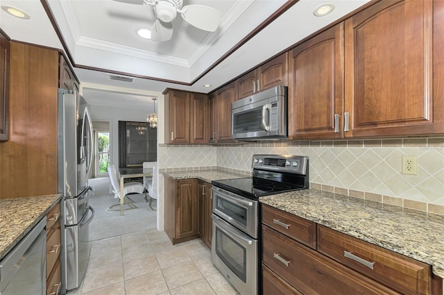 kitchen featuring a raised ceiling, light stone countertops, light tile patterned floors, ornamental molding, and stainless steel appliances