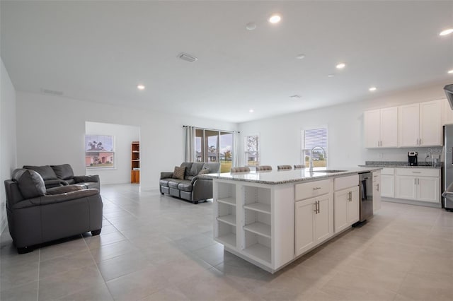 kitchen with white cabinetry, light stone countertops, sink, a center island with sink, and light tile patterned flooring