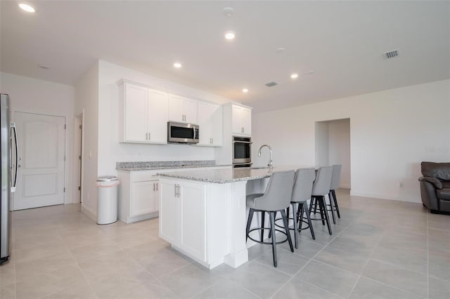 kitchen with light stone counters, light tile patterned flooring, an island with sink, white cabinets, and appliances with stainless steel finishes