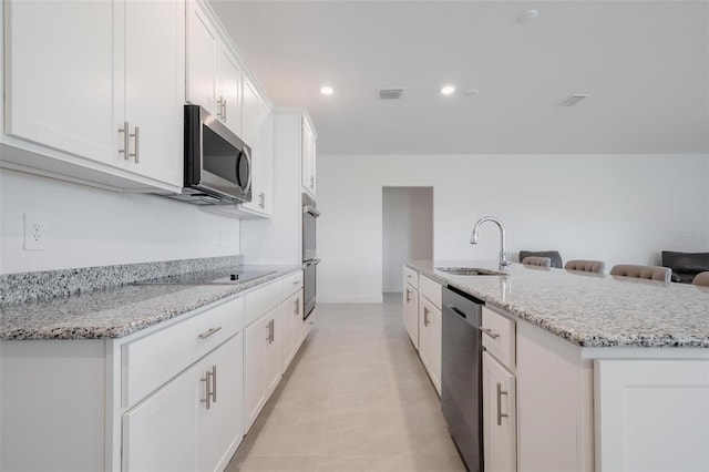 kitchen featuring sink, stainless steel appliances, light stone counters, a center island with sink, and white cabinets