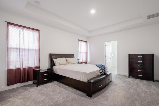 bedroom featuring connected bathroom, light colored carpet, and a tray ceiling