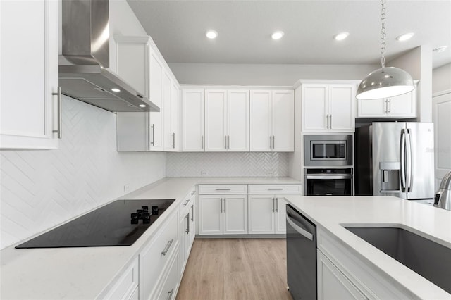 kitchen with white cabinets, wall chimney exhaust hood, hanging light fixtures, and appliances with stainless steel finishes