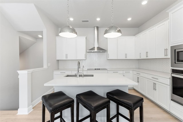 kitchen with a sink, visible vents, a kitchen breakfast bar, wall chimney range hood, and light wood-type flooring