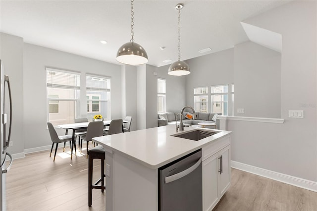 kitchen featuring stainless steel appliances, a sink, light wood-style floors, hanging light fixtures, and light countertops