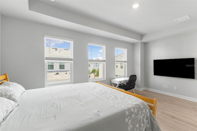 bedroom with light hardwood / wood-style floors and a tray ceiling