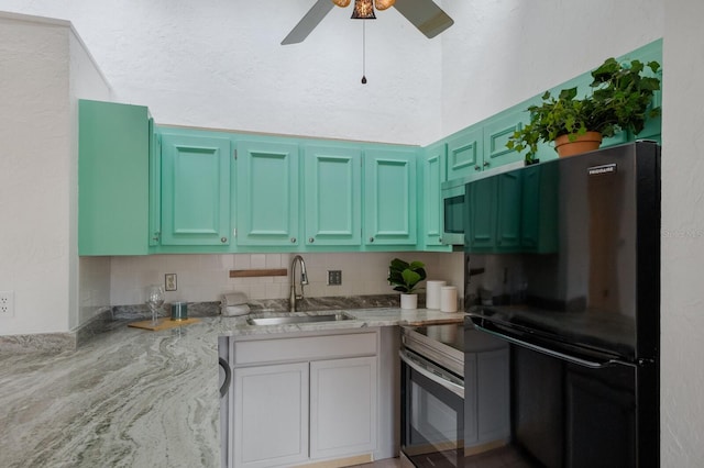 kitchen featuring black refrigerator, sink, stainless steel stove, tasteful backsplash, and light stone counters