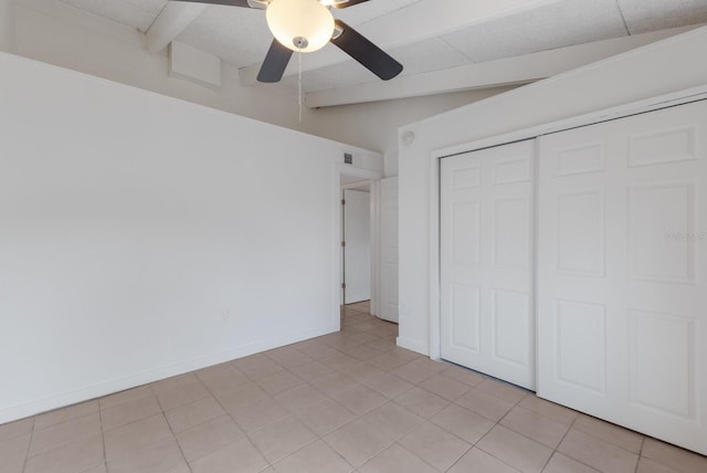 unfurnished bedroom featuring ceiling fan, a closet, light tile patterned floors, and lofted ceiling with beams