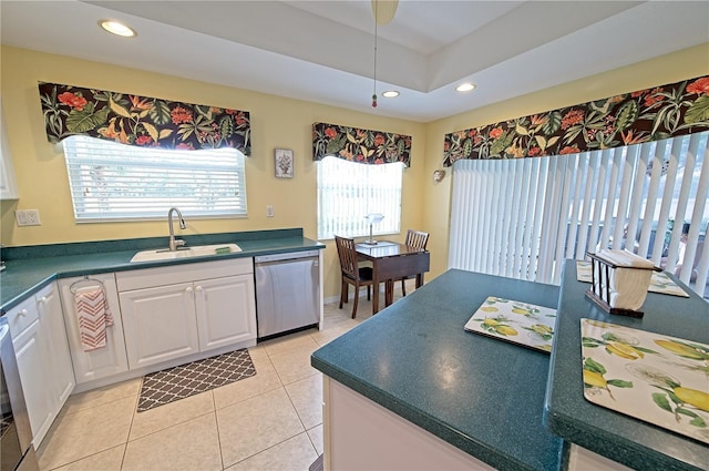 kitchen featuring sink, light tile patterned floors, stainless steel dishwasher, a tray ceiling, and white cabinets