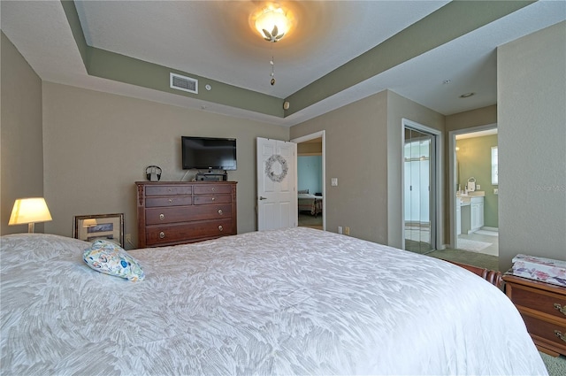 bedroom featuring carpet, a raised ceiling, and ensuite bath