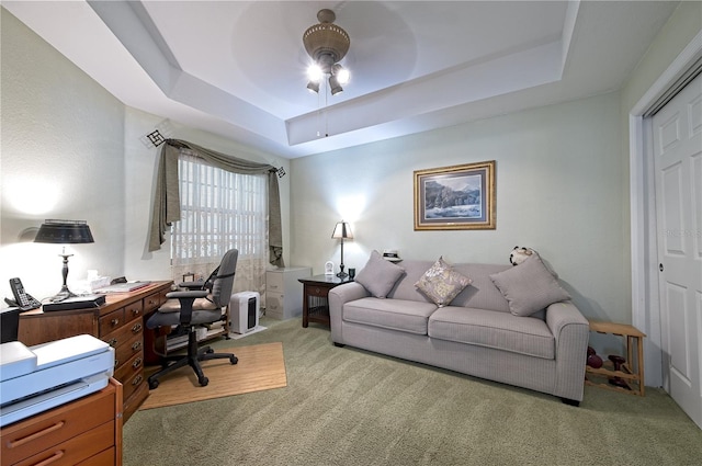 carpeted office space featuring a tray ceiling and ceiling fan