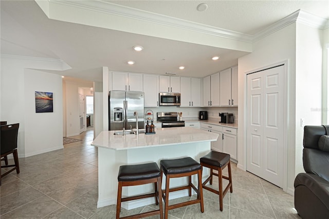 kitchen with appliances with stainless steel finishes, a kitchen bar, a center island with sink, white cabinets, and ornamental molding