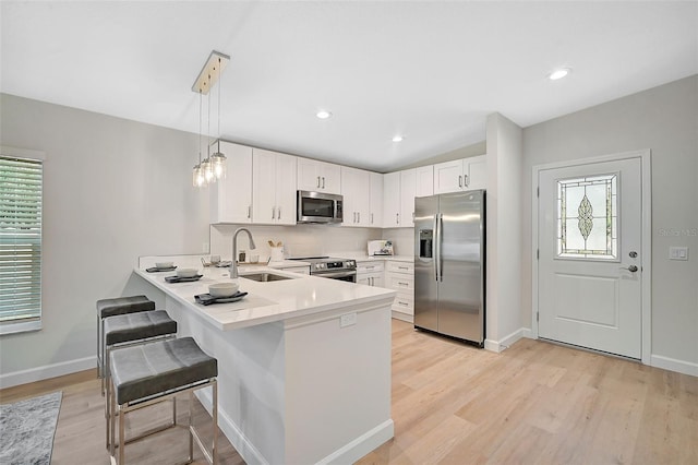 kitchen featuring a breakfast bar, white cabinets, hanging light fixtures, appliances with stainless steel finishes, and kitchen peninsula