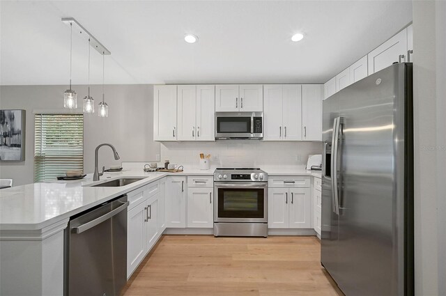 kitchen with kitchen peninsula, stainless steel appliances, sink, pendant lighting, and white cabinetry