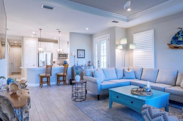 living room with light wood-type flooring, ornamental molding, and a tray ceiling