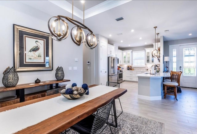 dining space with an inviting chandelier, crown molding, sink, a tray ceiling, and light hardwood / wood-style floors