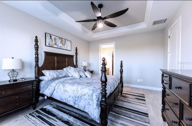 bedroom featuring ceiling fan, a raised ceiling, light wood-type flooring, and ornamental molding