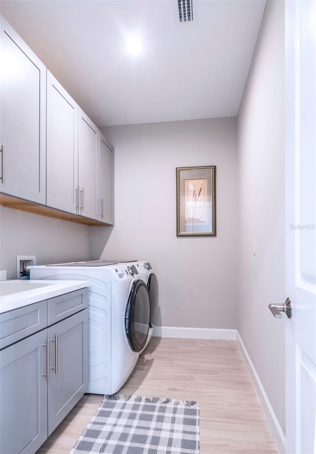 clothes washing area featuring cabinets, separate washer and dryer, and light hardwood / wood-style floors