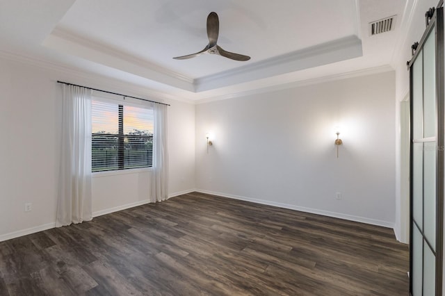 empty room featuring a barn door, dark wood-type flooring, crown molding, and a tray ceiling