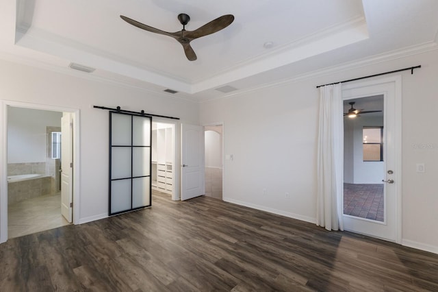 unfurnished bedroom with dark wood-type flooring, a raised ceiling, ensuite bath, ceiling fan, and a barn door