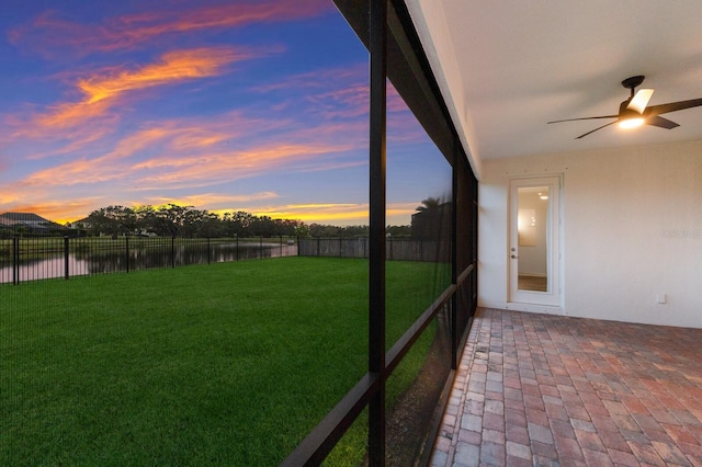 yard at dusk with ceiling fan, a patio area, and a water view