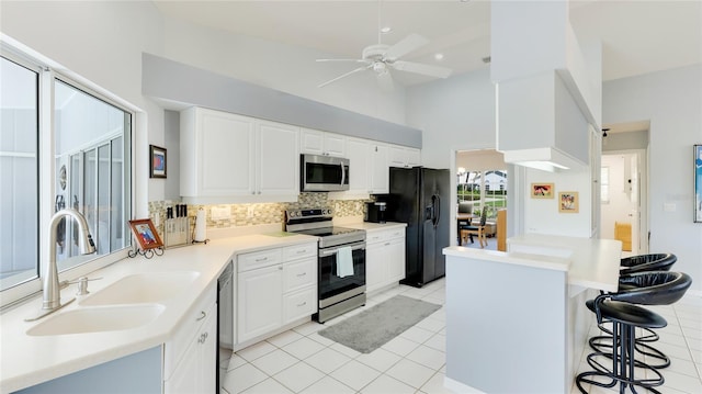 kitchen with white cabinets, sink, light tile patterned floors, appliances with stainless steel finishes, and a breakfast bar area