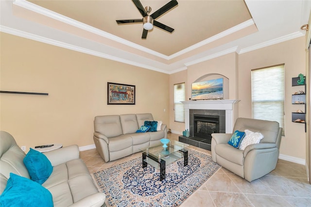 tiled living room featuring a raised ceiling, ceiling fan, ornamental molding, and a tiled fireplace