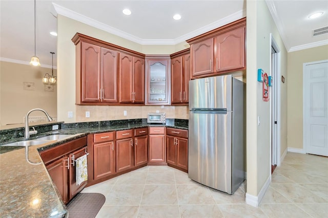 kitchen featuring sink, hanging light fixtures, dark stone countertops, crown molding, and stainless steel fridge