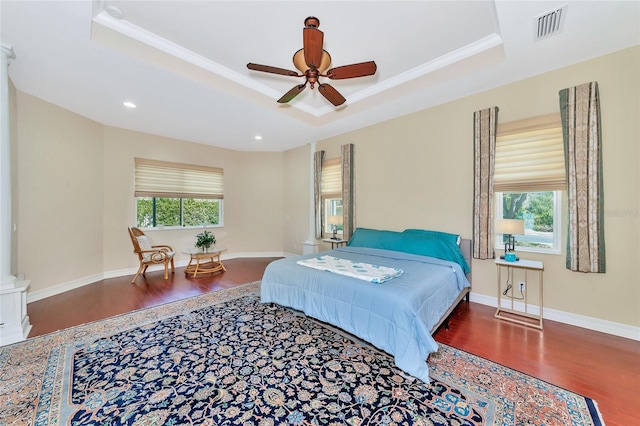 bedroom featuring hardwood / wood-style flooring, ceiling fan, a raised ceiling, and multiple windows