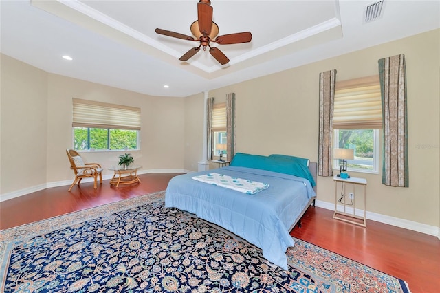 bedroom featuring hardwood / wood-style flooring, multiple windows, a tray ceiling, and ceiling fan