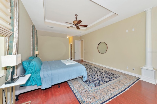 bedroom featuring hardwood / wood-style floors, ceiling fan, ornate columns, and a tray ceiling