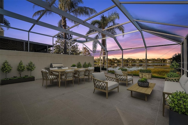 patio terrace at dusk with glass enclosure, a water view, and an outdoor hangout area