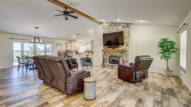 living room featuring lofted ceiling with beams, light hardwood / wood-style floors, a stone fireplace, and ceiling fan with notable chandelier