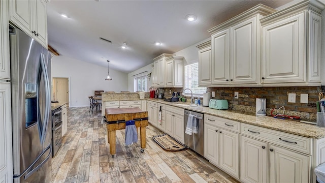 kitchen featuring light stone countertops, appliances with stainless steel finishes, pendant lighting, light hardwood / wood-style flooring, and lofted ceiling