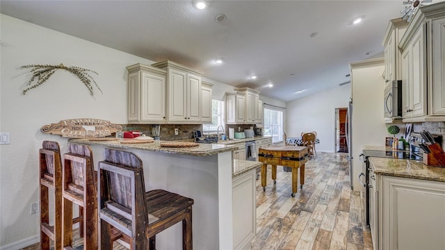 kitchen with tasteful backsplash, a kitchen bar, light hardwood / wood-style floors, and lofted ceiling