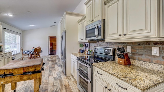 kitchen with light stone countertops, appliances with stainless steel finishes, light wood-type flooring, and cream cabinetry