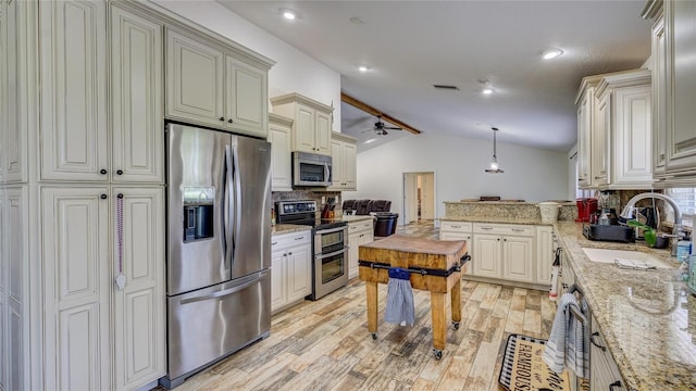 kitchen with light stone countertops, sink, hanging light fixtures, vaulted ceiling, and appliances with stainless steel finishes