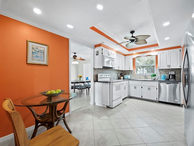 kitchen with a raised ceiling, crown molding, white cabinetry, and stainless steel appliances