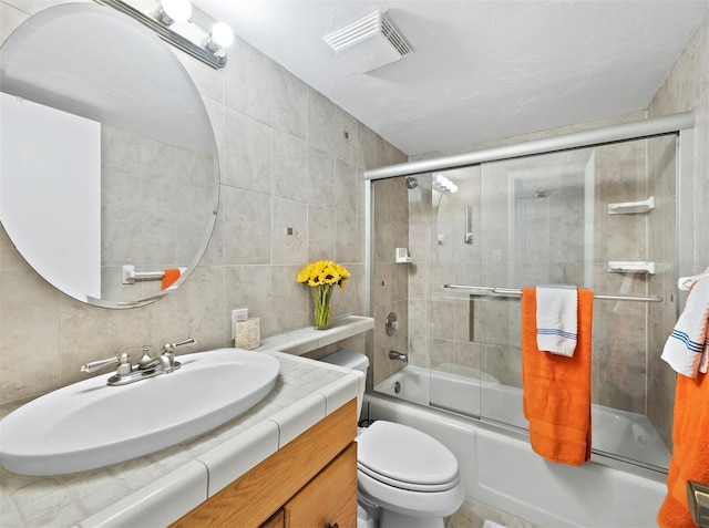 full bathroom with tasteful backsplash, bath / shower combo with glass door, vanity, tile walls, and toilet