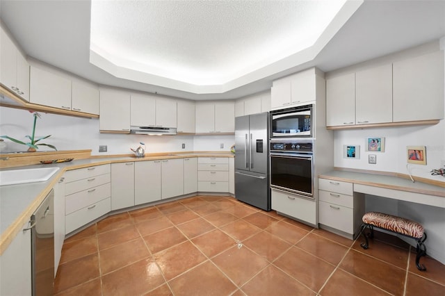 kitchen featuring stainless steel appliances, white cabinets, a textured ceiling, a tray ceiling, and light tile patterned flooring