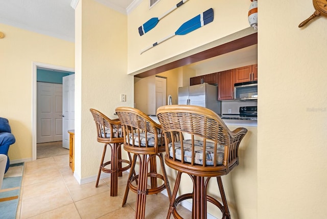 kitchen with a kitchen bar, light tile patterned floors, stainless steel appliances, and ornamental molding