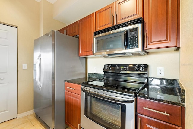 kitchen featuring appliances with stainless steel finishes, light tile patterned floors, and dark stone countertops