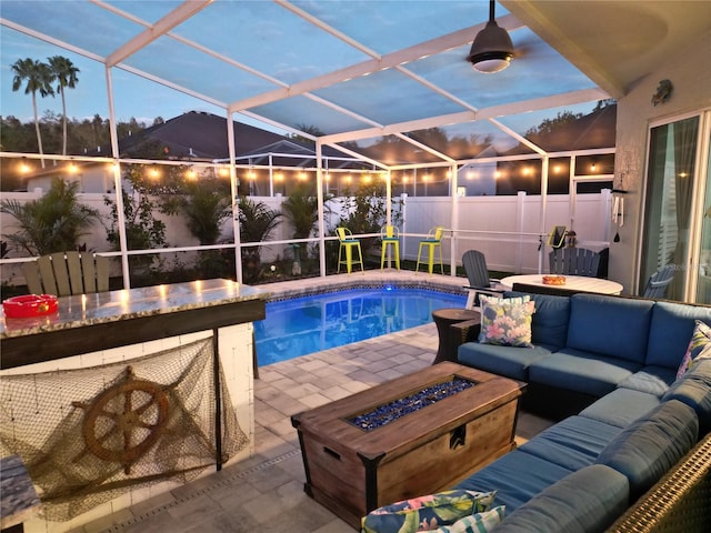 pool at dusk featuring glass enclosure, a patio, and an outdoor living space with a fire pit