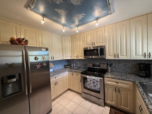 kitchen featuring sink, appliances with stainless steel finishes, dark stone countertops, light tile patterned flooring, and decorative backsplash