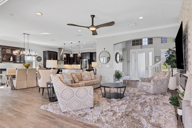 living room featuring ceiling fan, sink, light wood-type flooring, and ornamental molding