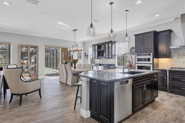 kitchen with stainless steel appliances, pendant lighting, a kitchen island with sink, a breakfast bar, and light wood-type flooring