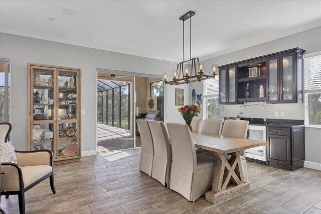 dining area with a healthy amount of sunlight, light hardwood / wood-style floors, beverage cooler, and an inviting chandelier