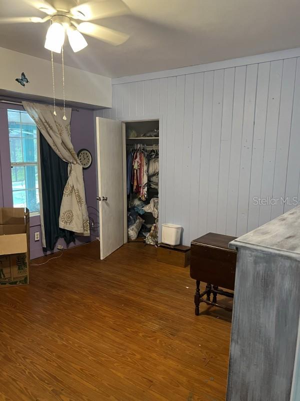 bedroom featuring a closet, ceiling fan, hardwood / wood-style floors, and wood walls