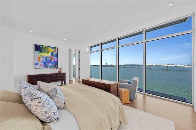 bedroom featuring access to outside, floor to ceiling windows, a water view, and wood-type flooring