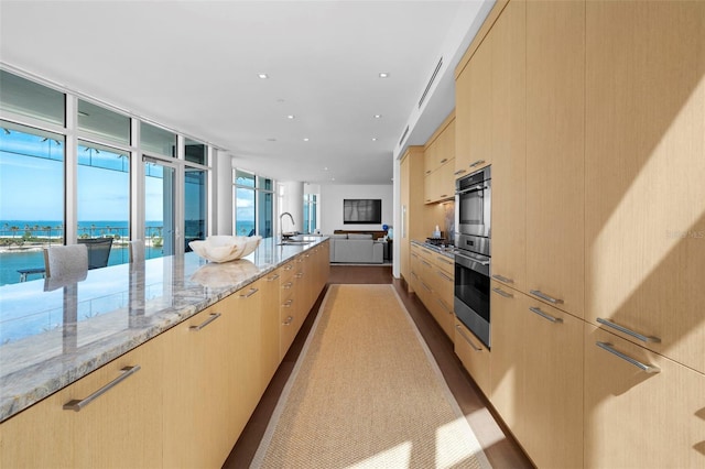 kitchen with light brown cabinets, a water view, light stone countertops, and light hardwood / wood-style flooring