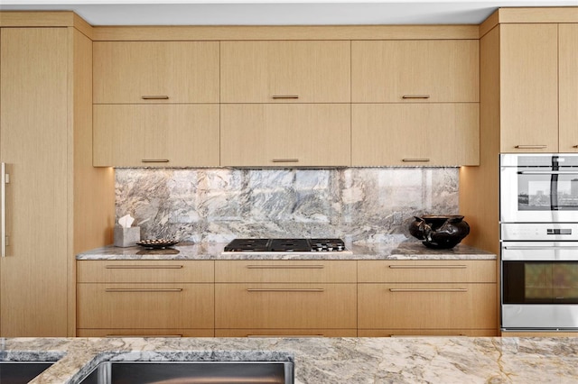 kitchen featuring double oven, backsplash, light brown cabinets, and gas cooktop